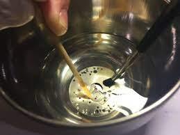 A man is clean watch parts in a bowl of water with tools